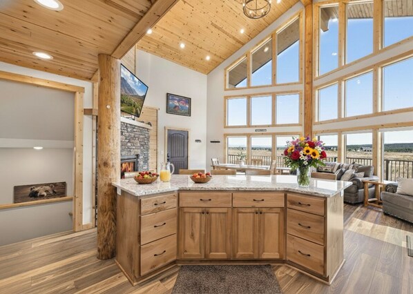 A spacious kitchen with wooden cabinets, a granite countertop, and large windows offering a view of the outdoors.