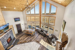 Amplia sala de estar con chimenea, mesa de comedor y ventanas grandes que ofrecen vistas al exterior.
