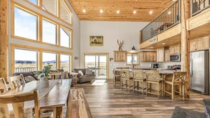 A spacious kitchen with wooden cabinets, a dining area with a large table, and a view of the mountains through large windows. - Eagle Eye Retreat (Island Park)