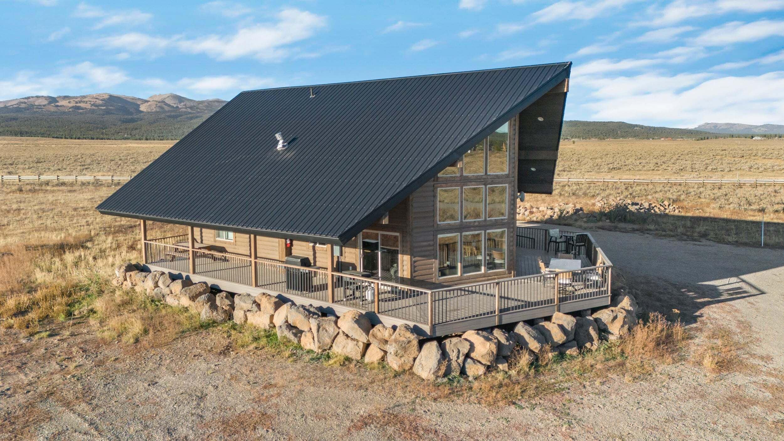 A log cabin with a sloped roof, large windows, and a deck with outdoor seating.