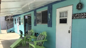 A building with a teal exterior, a door labeled 'Captain's Quarters,' and two green Adirondack chairs outside.