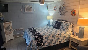 A bedroom with a bed, a ceiling fan, a wall-mounted air conditioner, a TV, and nautical-themed decorations.