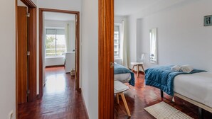 Une chambre d’hôtel avec un plancher en bois, un lit recouvert d’une couverture bleue, une chaise, une petite table et une fenêtre avec des rideaux.