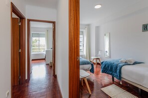 Ein Hotelzimmer mit Holzboden, einem Bett mit blauer Decke, einem Stuhl, einem kleinen Tisch und einem Fenster mit Vorhängen.