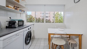 Une cuisine compacte équipée d’un lave-linge, d’un four à micro-ondes et d’un coin repas avec une table et des chaises.