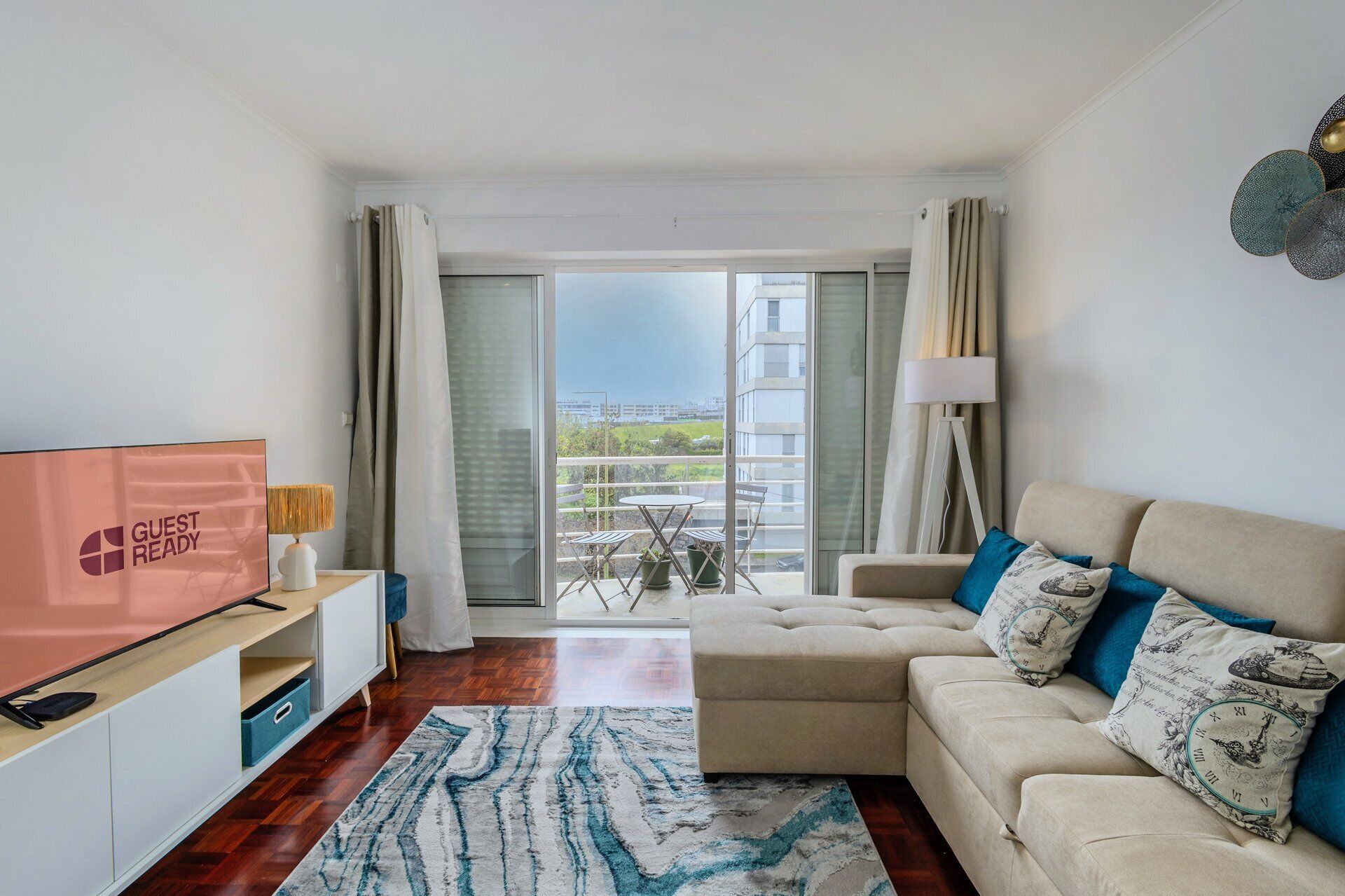 A modern living room with a sofa, a TV, a lamp, and a view of the city through large windows.
