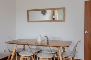 Ein Essbereich mit einem Holztisch, sechs Stühlen, einer weißen Karaffe, einer Flasche und einem gerahmten Spiegel an der Wand.