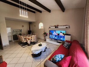 Ein Wohnzimmer mit Fernseher, einem roten Sofa und einem Essbereich mit Tisch und Stühlen.