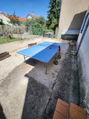 An outdoor ping pong table with a net, surrounded by gravel and a concrete floor, with a building and trees in the background. - Le Ciel Bleu, located a 10-minute walk from the historic center of Arles and the train station (Arles)