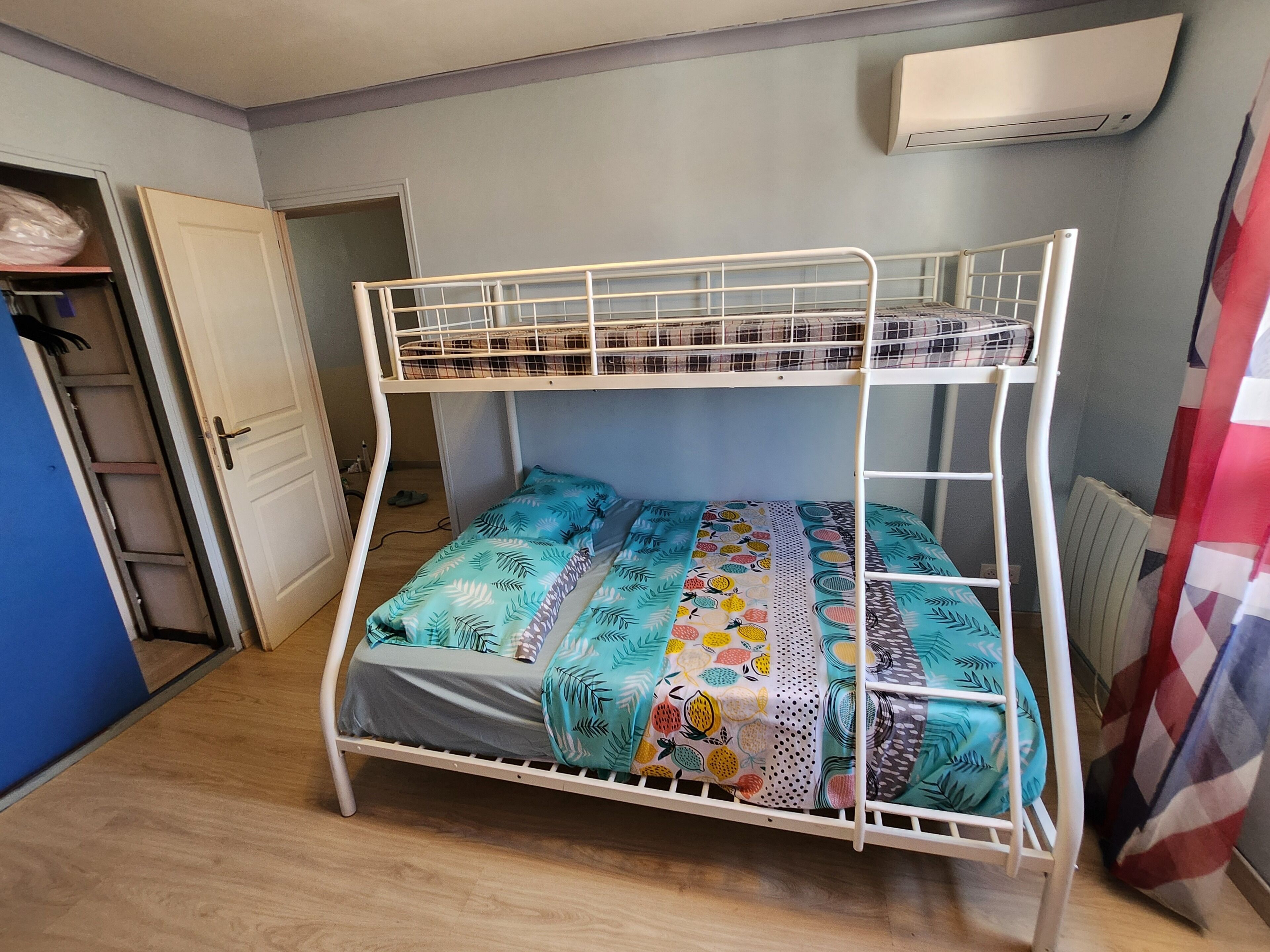 Un lit superposé avec une couvre-lit à motifs, une porte, un radiateur et un mur bleu.