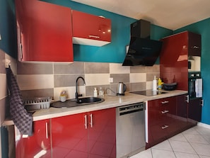 Una cocina moderna con armarios rojos, un lavavajillas de acero inoxidable y una campana extractora negra.