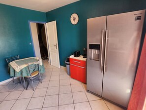 A compact kitchen with a stainless steel refrigerator, a red cabinet, and a dining table with chairs. - Le Ciel Bleu, located a 10-minute walk from the historic center of Arles and the train station (Arles)