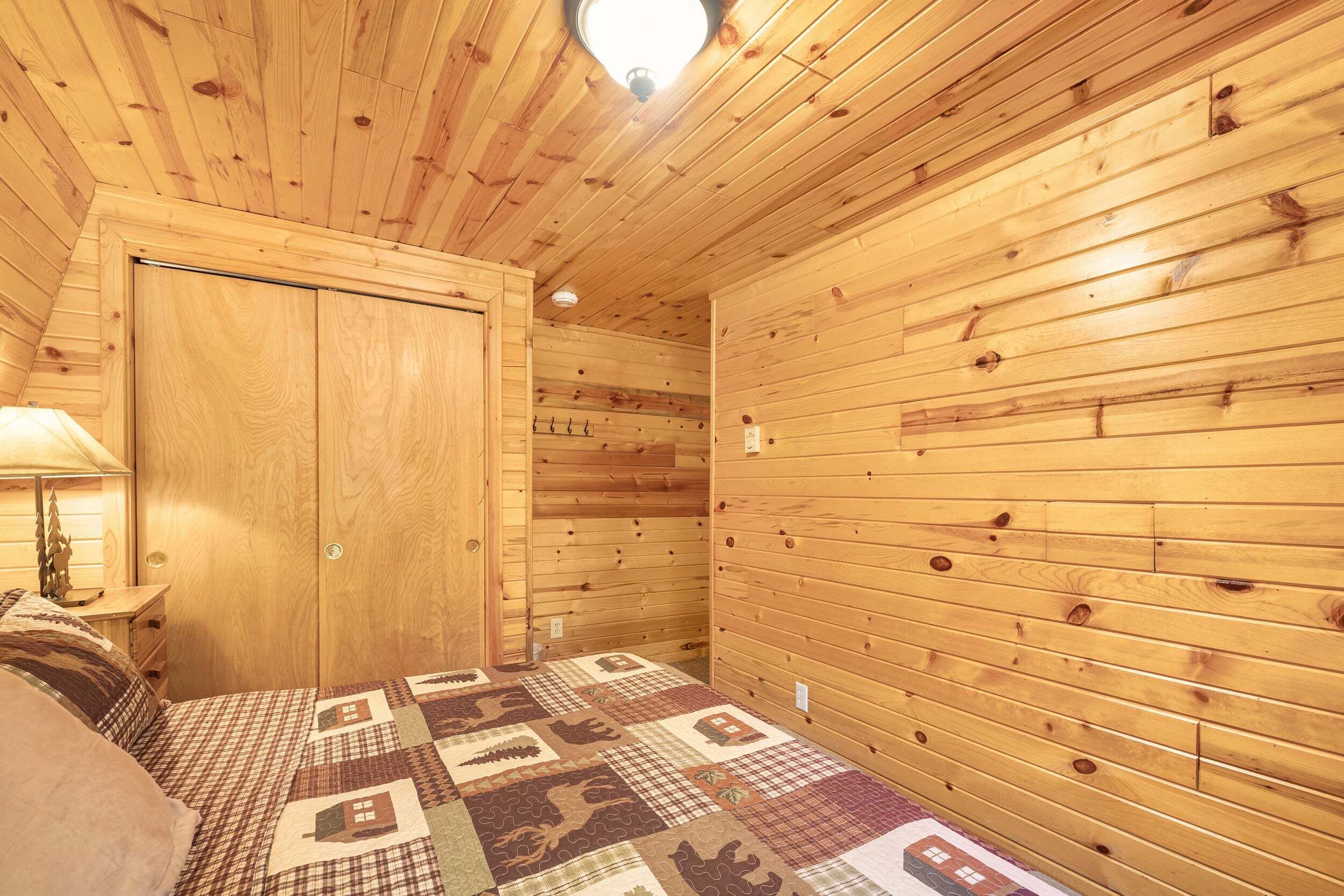 A wooden-paneled room with a bed, a nightstand, and a wall-mounted lamp.