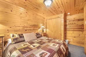 Ein Zimmer mit Holzwänden, einem Bett, einem Nachttisch, einer Lampe und einem Kleiderschrank.