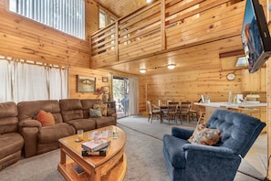 A wooden interior with a sofa, armchair, dining table, and a TV mounted on the wall.