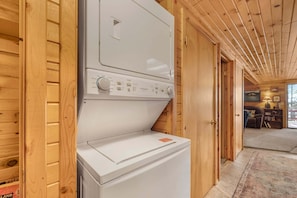 A laundry room with a washer and dryer, wooden walls, and a door leading to a living area.