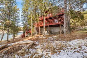 A cabin with a red exterior, situated on stilts among trees, overlooking a body of water. - Lakeside Brimwater (Island Park)