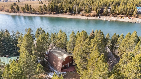 A cabin with a sloped roof, surrounded by dense pine trees, near a calm lake.