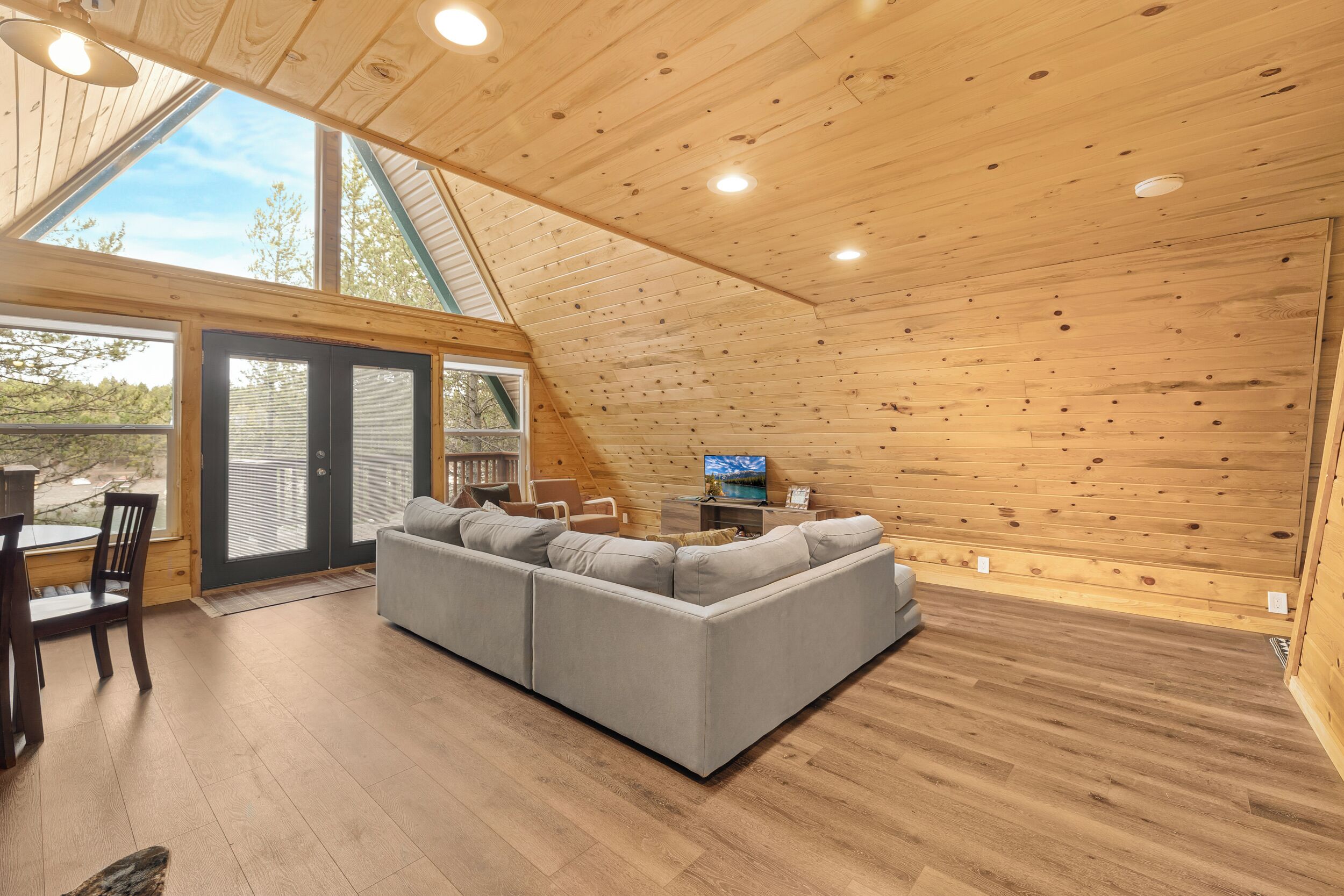 A modern log cabin interior with a sectional sofa, dining table, chairs, and a TV.
