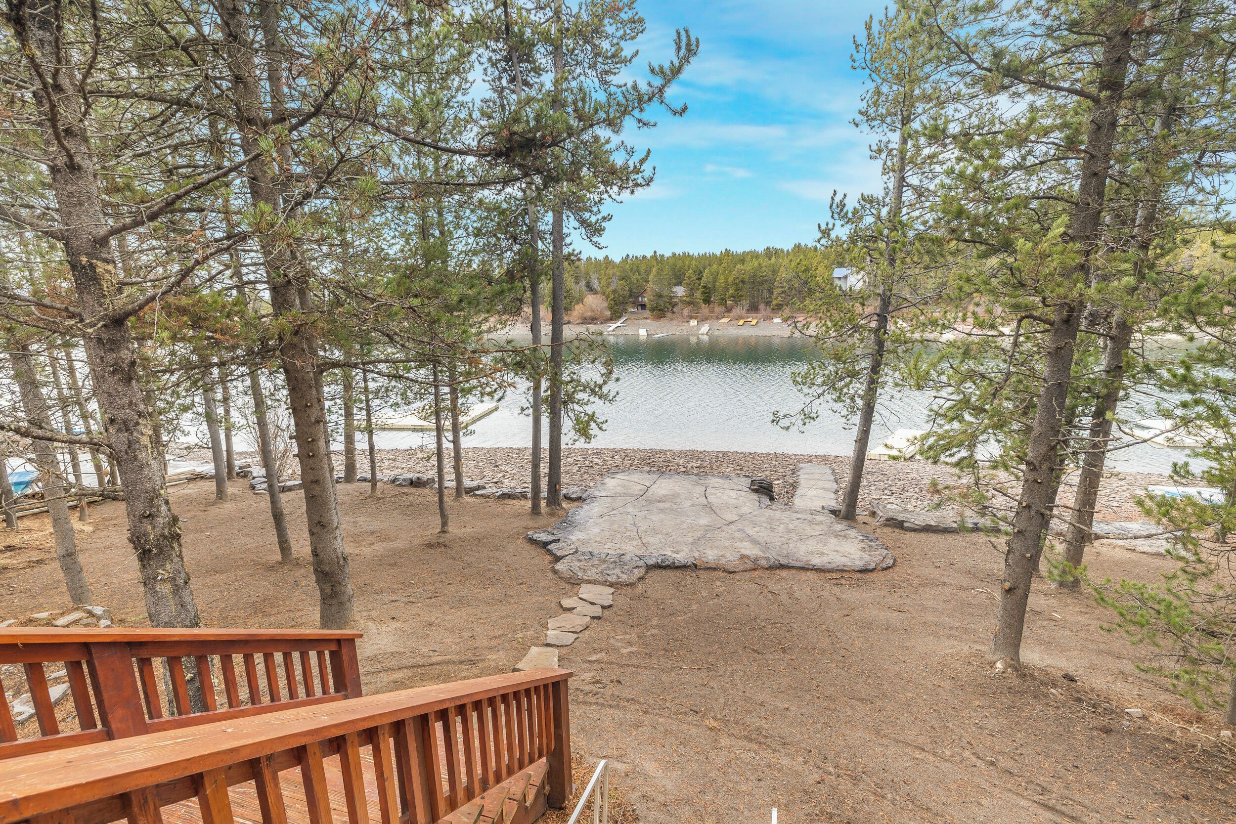 Una terraza de madera que lleva a un lago con árboles y un sendero de piedra.