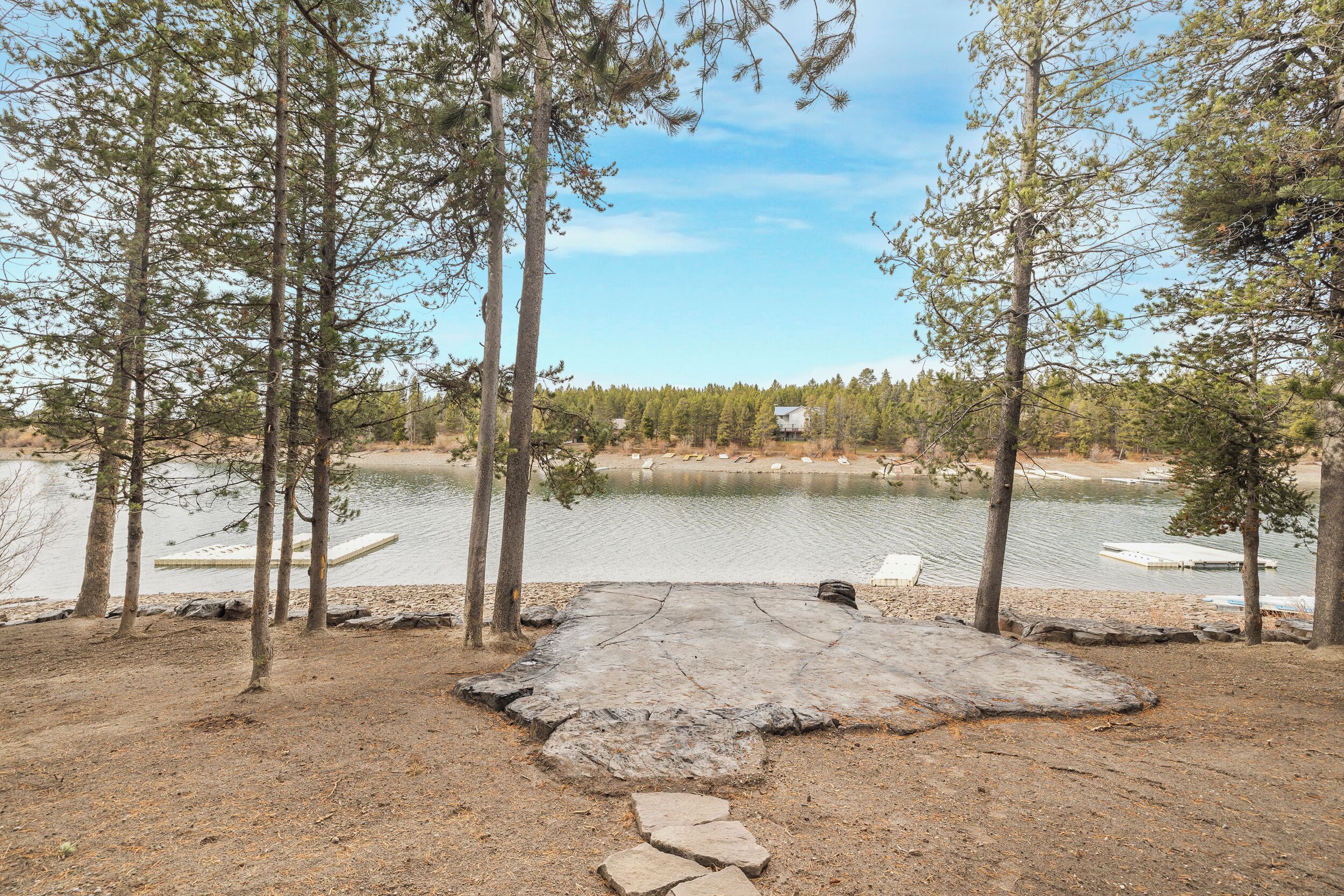 A lakeside view with a stone platform, trees, and docked boats.