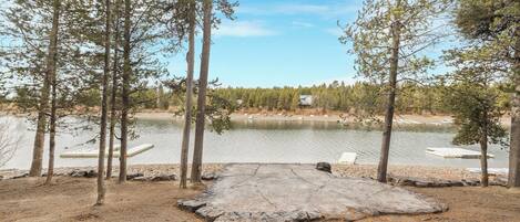 Vista de un lago con una plataforma de piedra, árboles y barcos amarrados.