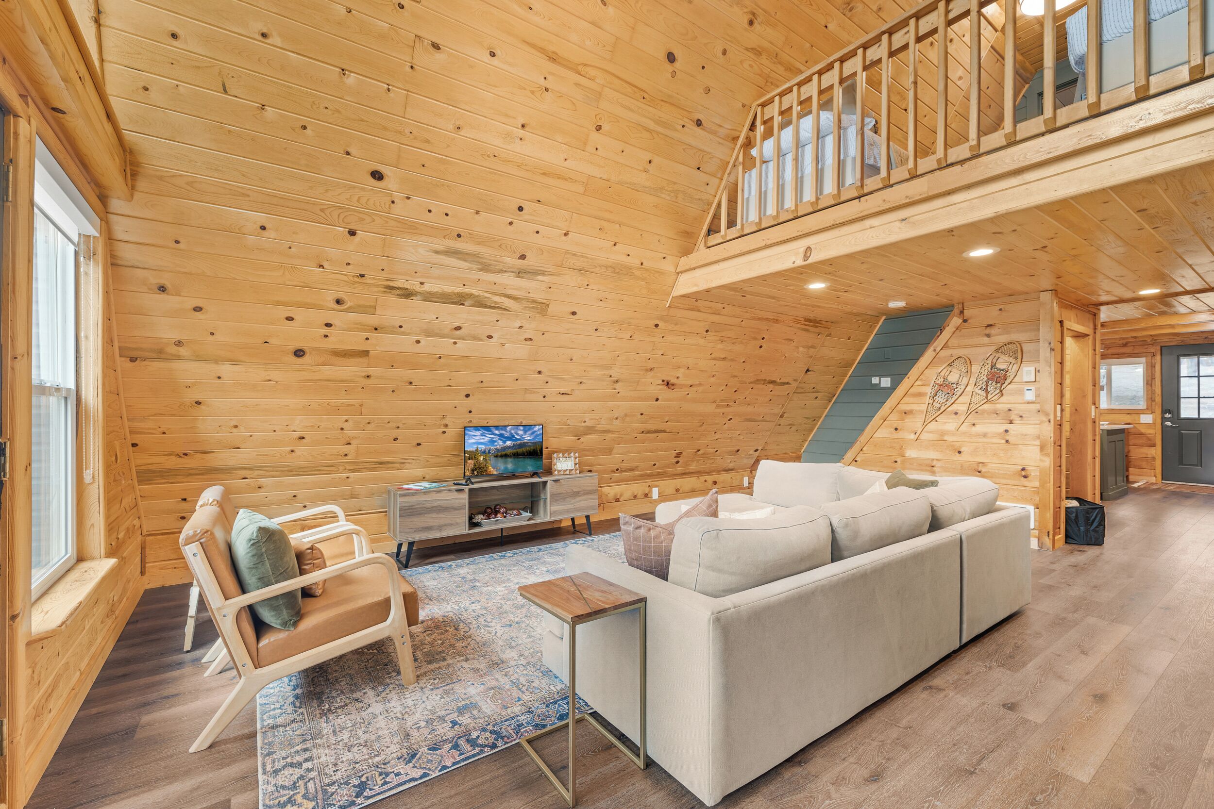 A wooden interior with a sofa, a TV, a staircase, and a window.