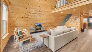 Un intérieur en bois avec un canapé, un téléviseur, un escalier et une fenêtre.
