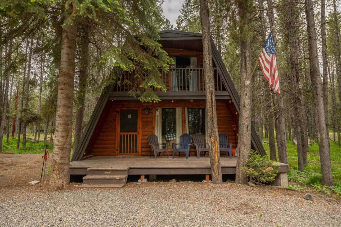 A cabin with a porch, two levels, and an American flag.