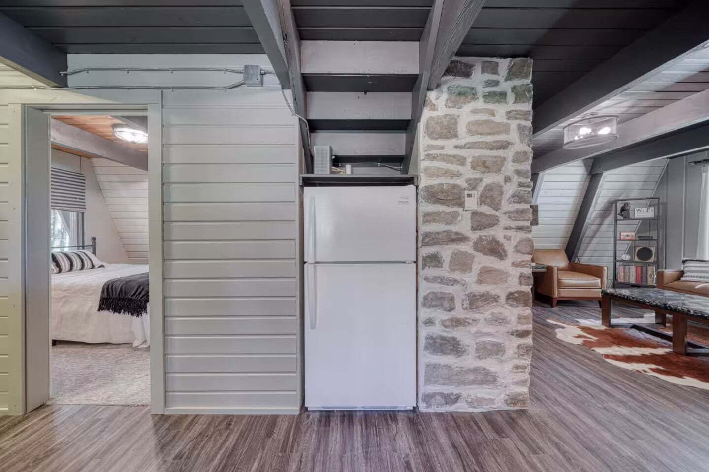 A compact room with a built-in refrigerator, a stone accent wall, and a cozy seating area with a leather armchair and a small table.
