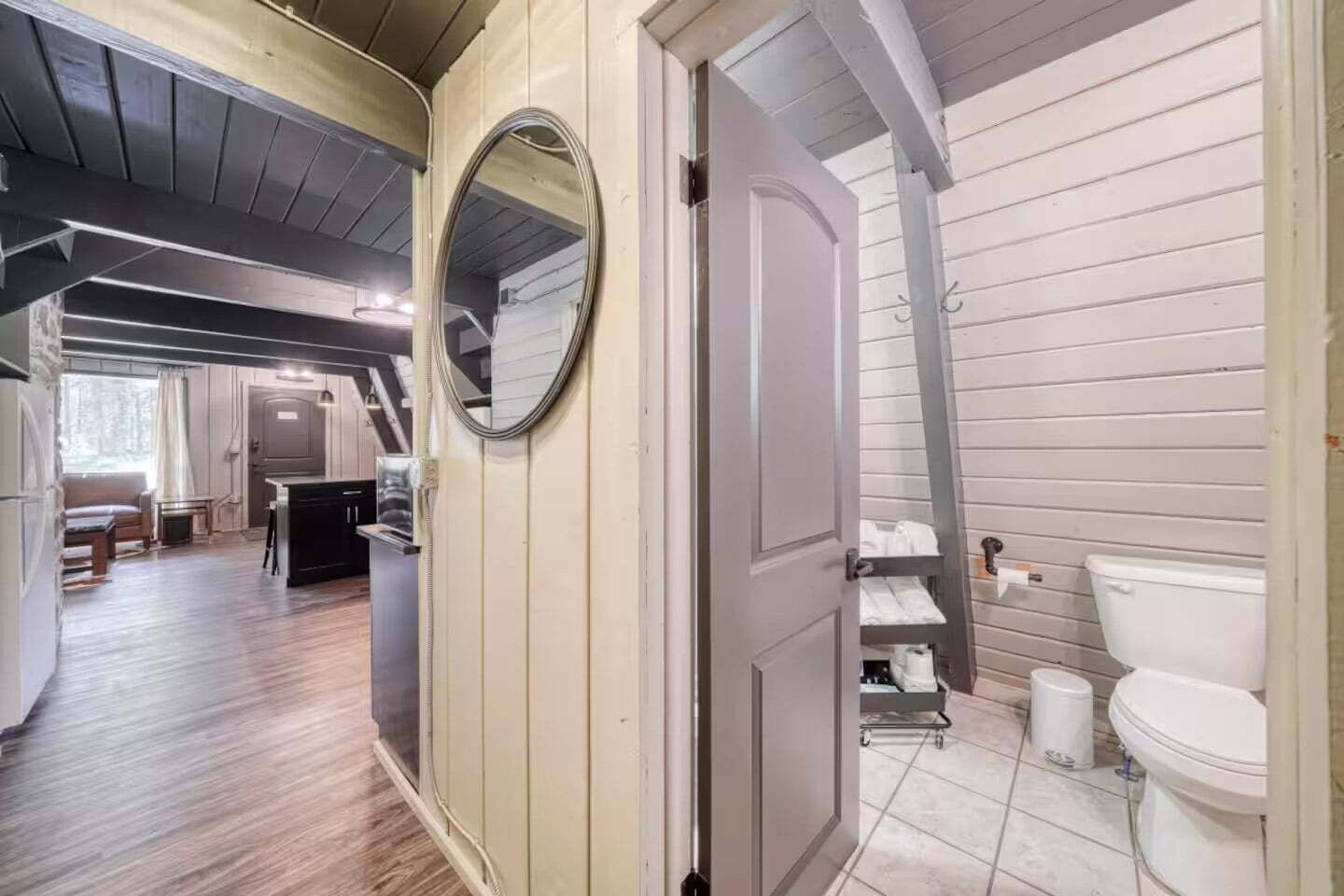 Une petite cabane compacte, composée d’une seule pièce, comprenant un coin cuisine, un petit espace repas et une salle de bain avec des toilettes et des étagères.