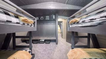 A bunk bed room with a central bench, storage baskets, and a hallway leading to another room.