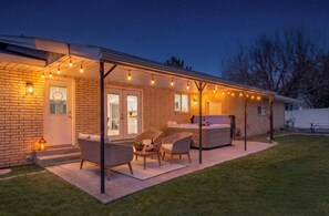 A covered patio with outdoor seating, a hot tub, and string lights.