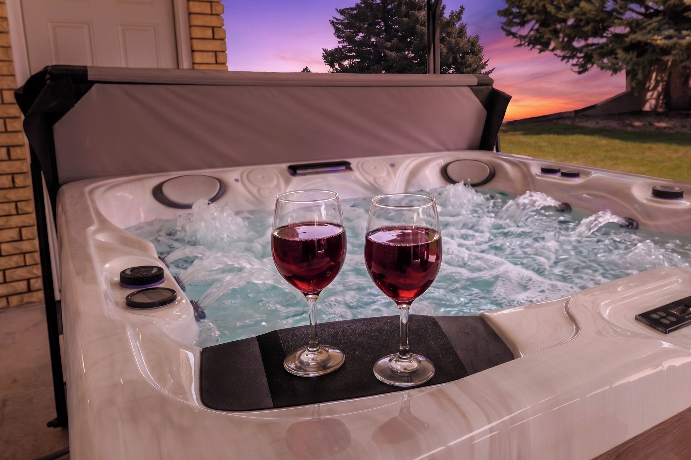 A hot tub with two glasses of red wine on the edge.