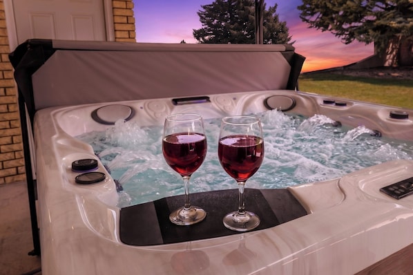 A hot tub with two glasses of red wine on the edge.