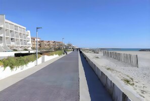 Un paseo marítimo costero con un camino de hormigón, playa y edificios modernos.