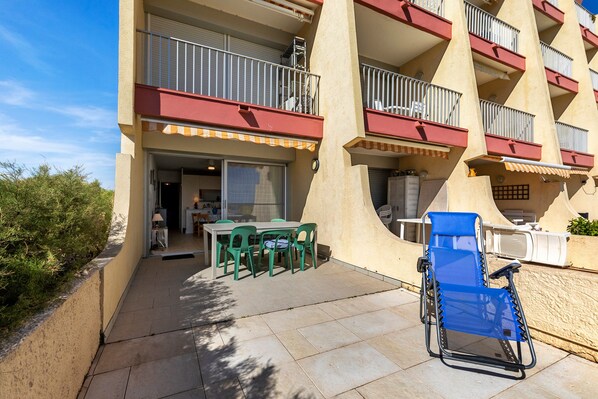 A hotel balcony with outdoor seating, a pool, and a clear sky.