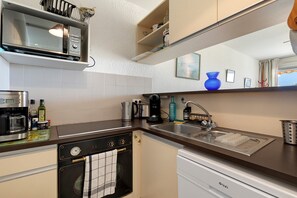A compact kitchen with a microwave, coffee maker, kettle, and dishwasher.