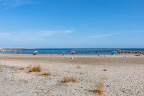 A beach with people sunbathing and swimming, a rocky shoreline, and a clear blue sky.