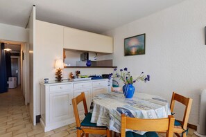 A compact kitchen with white cabinets, a dining table with chairs, and a vase with flowers on the table.