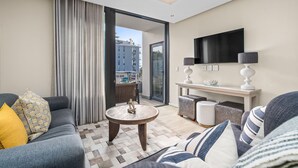Un salon moderne comprenant un canapé, une table basse ronde, un téléviseur fixé au mur et une porte-fenêtre coulissante donnant sur un balcon extérieur.