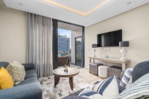 Ein modernes Wohnzimmer mit einer Couch, einem runden Couchtisch, einem an der Wand montierten Fernseher und einer Glastür zum Außenbereich.