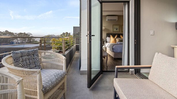 Un balcon doté de meubles en osier, une porte-fenêtre coulissante donnant sur une chambre à coucher avec un lit et un canapé.