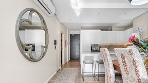 Une cuisine moderne avec des meubles blancs, un îlot central et un coin repas agrémenté d’un tapis à motifs et de tabourets de bar.