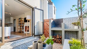 Een modern huis met een terras, een houten bankje, plantenpotten en een zichtbare keukenruimte.