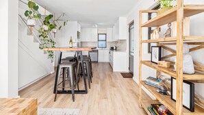 Een moderne keuken met een centraal eiland, barstoelen, hangende planten en een houten boekenkast.