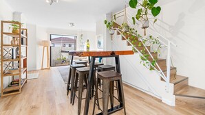 Een modern interieur met een houten eettafel, barstoelen, een trap en hangplanten.