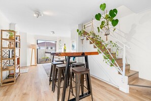Ein modernes Interieur mit einem Holzesstisch, Barhocker, einer Treppe und hängenden Pflanzen.