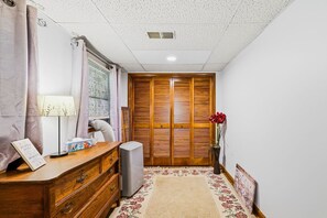 Een kamer met een houten kledingkast, een bureau met lamp, een prullenbak en een vloerkleed met bloemen.