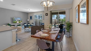 A modern dining area with a wooden table set for four, a bar area, and a sofa in the background. - Go!#32 CHAMPIONS GATE (Kissimmee)